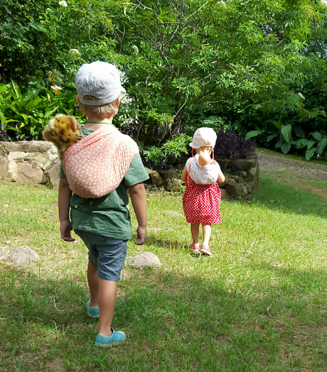 Milo und Ella tragen ihre Stofftiere und Puppen landestypisch auf dem Rücken.