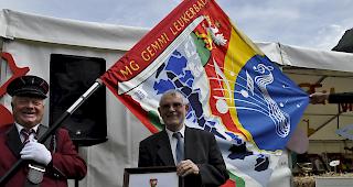 Pfarrer Perrig mit der Urkunde und der Fahne im Hintergrund.