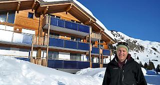 Gemeinderat Andreas Walker steht vor einem Geb&auml;ude, welches mit thermischen Solarkollektoren ausgestattet ist.