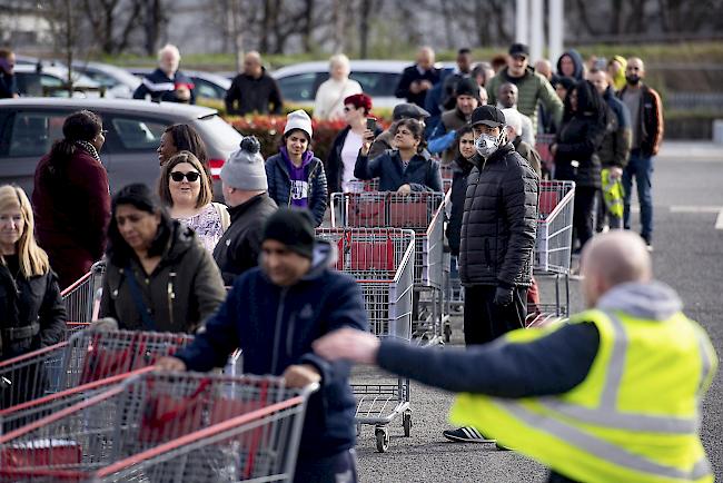 Menschen bilden eine lange Schlange, die sich weit um den Parkplatz schlängelt, während sie darauf warten, einen Grosshandels-Supermarkt in Coventry, England, zu betreten.